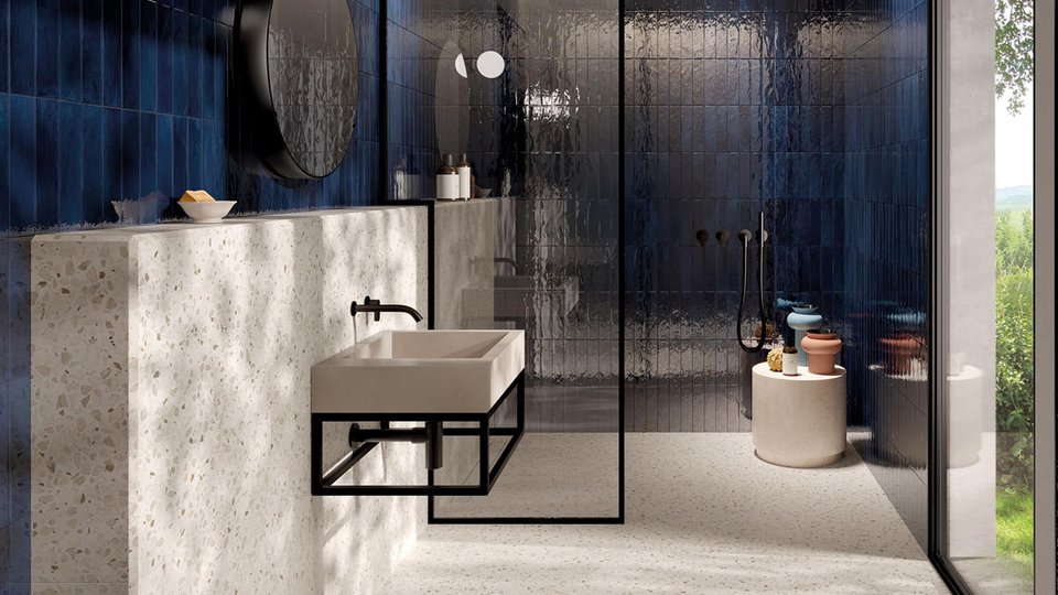 Modern bathroom with deep blue glossy wall tiles, wall-mounted washbasin in light stone and matt black metal details.