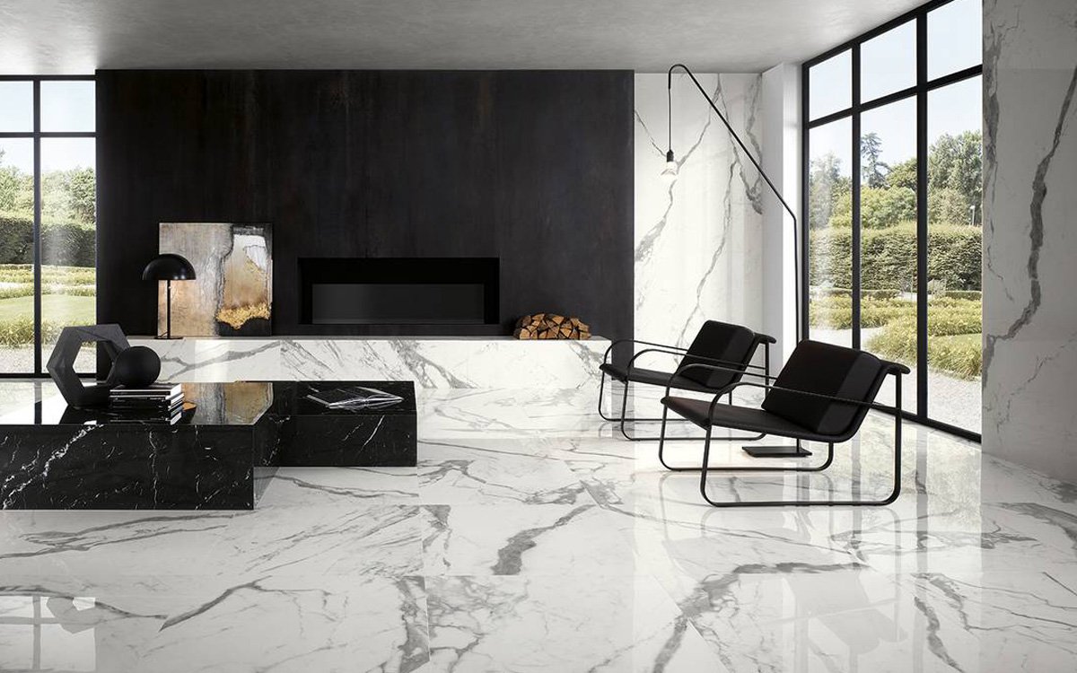 Modern living room with white veined marble effect walls and flooring, black furnishings and large windows that illuminate the space.