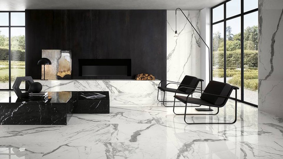 Modern living room with white veined marble effect walls and flooring, black furnishings and large windows that illuminate the space.