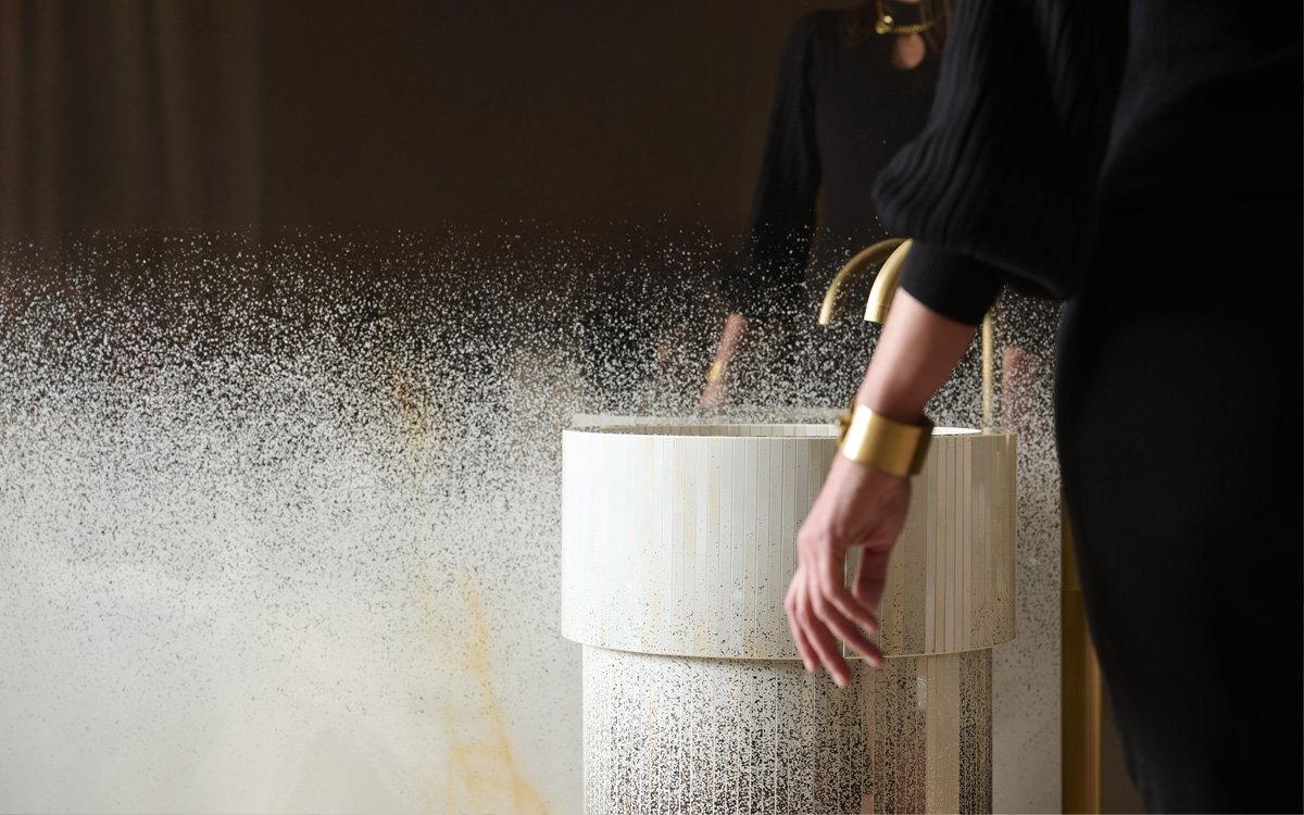 Cylindrical washbasin in light ceramic with gold tap, textured details and luminous reflections for a contemporary bathroom design.