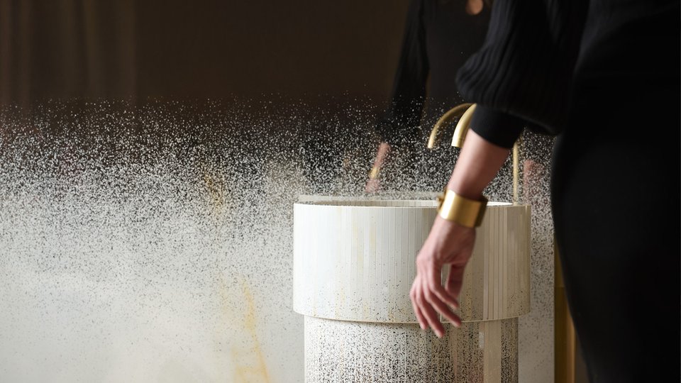 Цилиндрическая раковина из светлой керамики с золотым смесителем, фактурными деталями и светящимися отражениями для ванной комнаты в современном стиле.