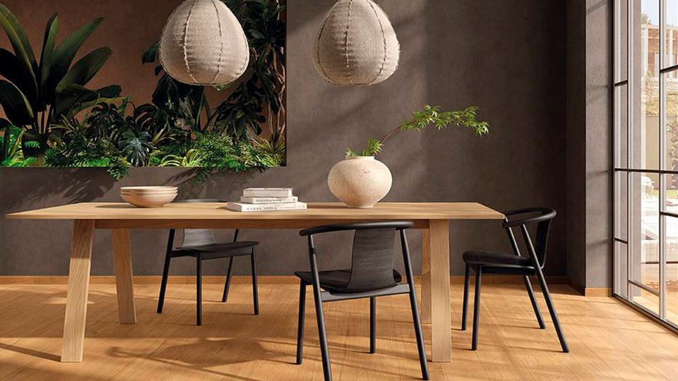 Modern dining area with light wood-effect flooring, mud-colored walls, and a large oak table, decorated with tropical plants.