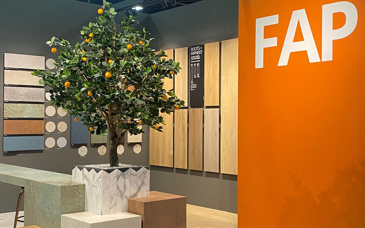 FAP Ceramiche stand with stone and wood effect panels, orange wall with logo and decorative tree with orange fruits.