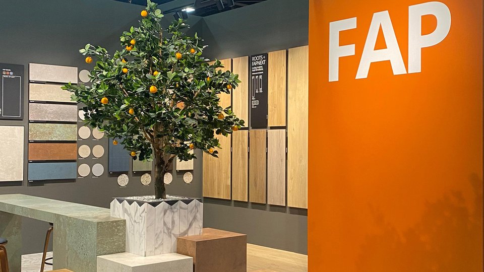 FAP Ceramiche stand with stone and wood effect panels, orange wall with logo and decorative tree with orange fruits.