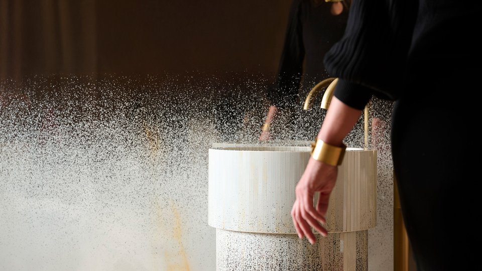 Cylindrical washbasin in light ceramic with gold tap, textured details and luminous reflections for a contemporary bathroom design.